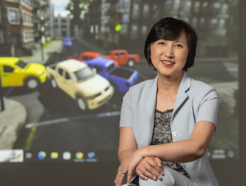 Gina Tang sits in front of a computer monitor showing an education game about traffic