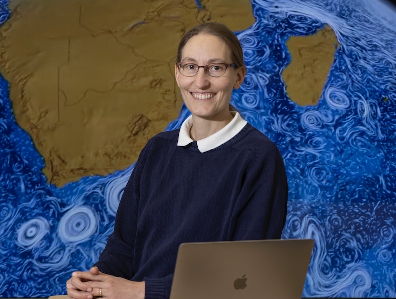 Rowan University professor Helga Huntley poses in front of a world map showing ocean transport patterns