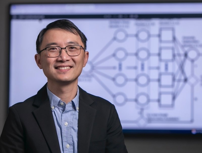 Professor Shen-Shyang-Ho stands in front of a computer screen with a graphic representation of data mining