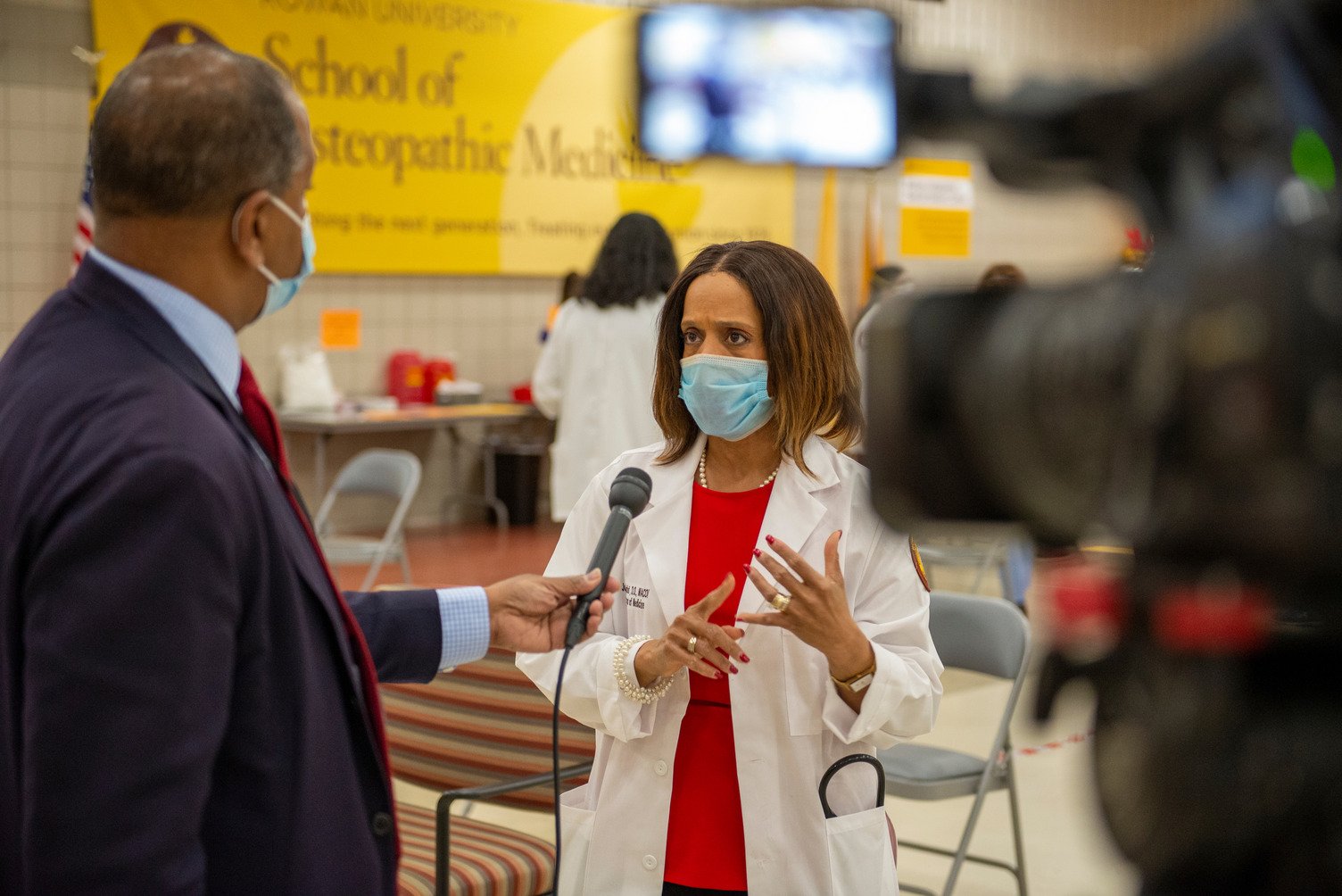 A woman in a medical mask and physician's coat speaks to a man holding a microphone