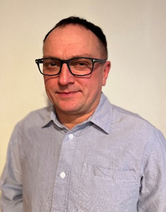 Dawid Wojtas, wearing glasses, smiles in front of a beige wall